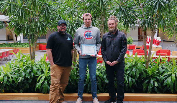Pinnacle Career Institute program director Jared Heitz (left), PCI graduate (center) holding a certificate, and instructor Blaine Pettipiece (right) standing together in the campus atrium.
