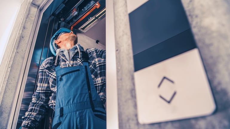 Elevator technician inspecting equipment above an open elevator doorway