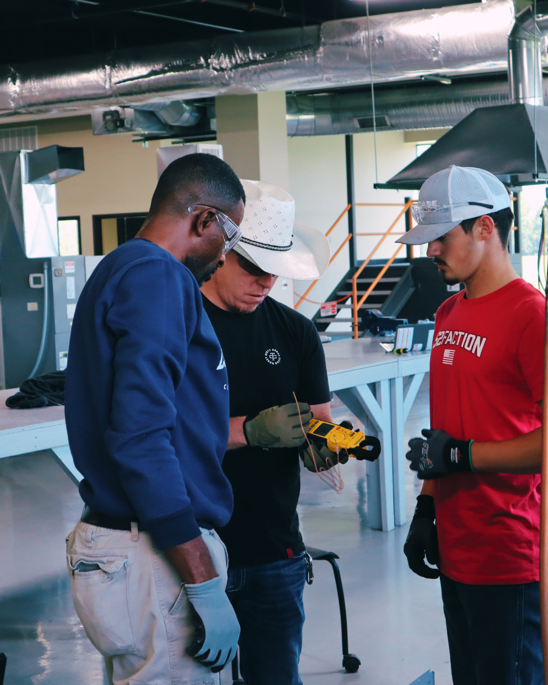 Two HVAC students reviewing equipment setup with an instructor during lab training.