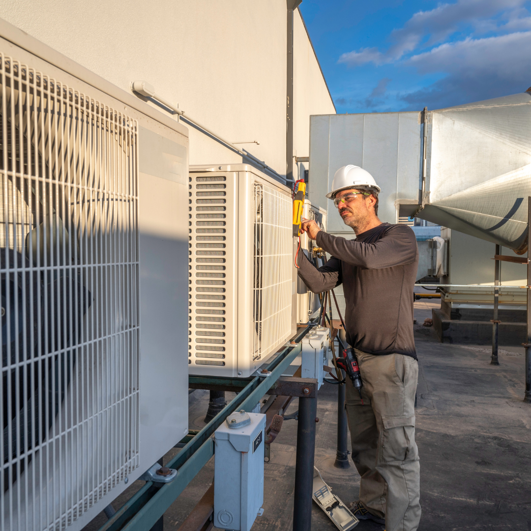 HVAC student servicing an outdoor air conditioning unit with safety gear and tools.
