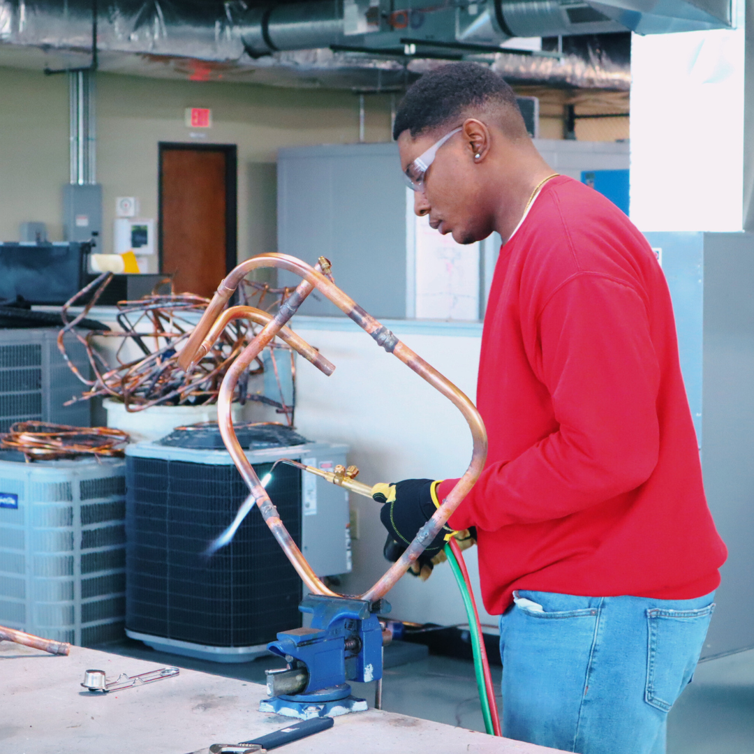 Student in red shirt working on HVAC wiring and copper tubing during trade school training.