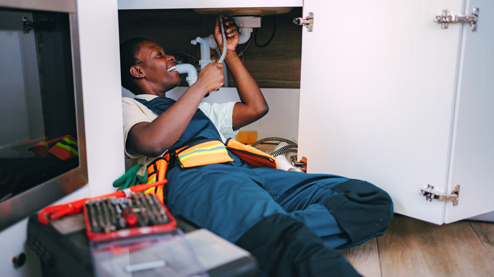 Plumber using a wrench to repair plumbing beneath a sink