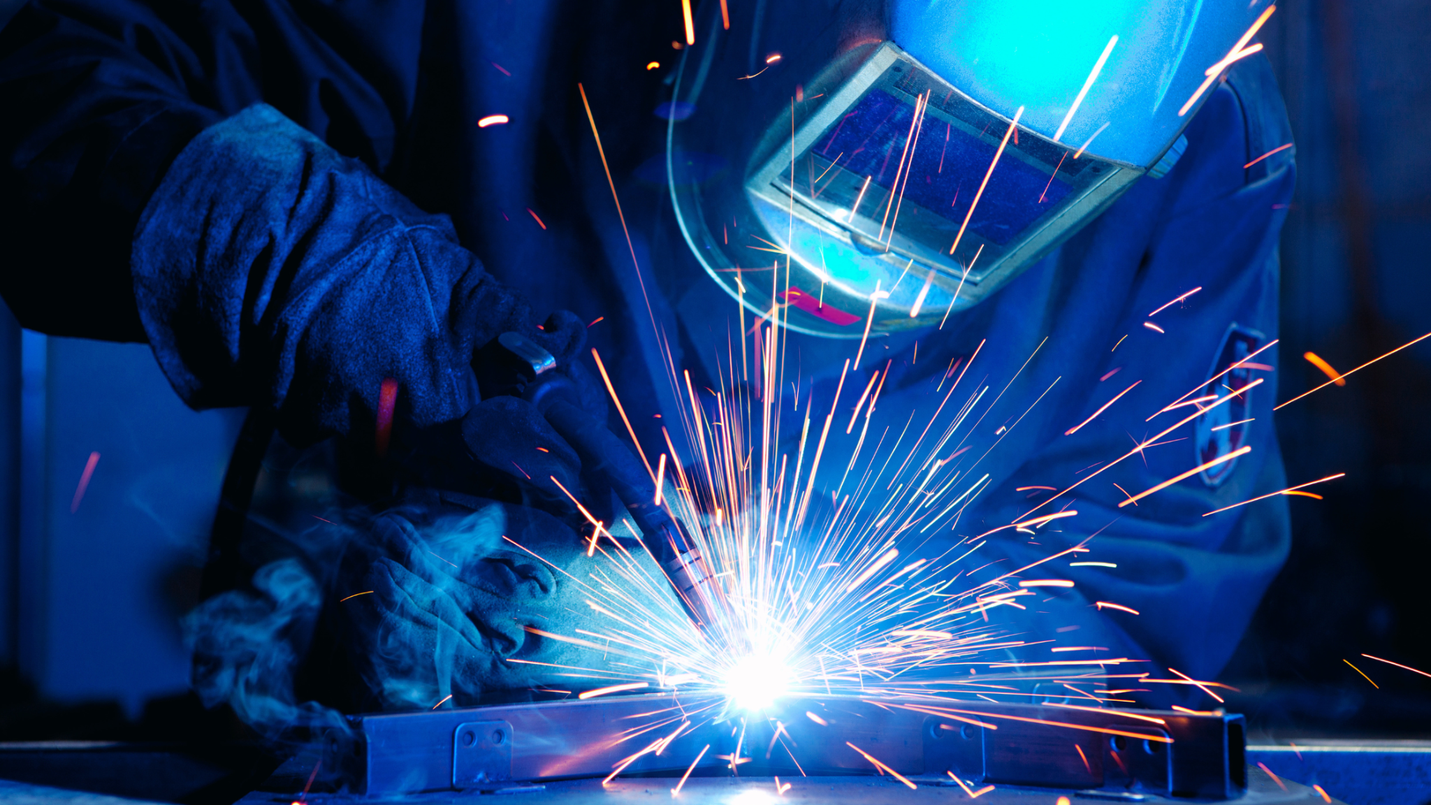 Welder wearing protective gear while welding metal and creating bright sparks