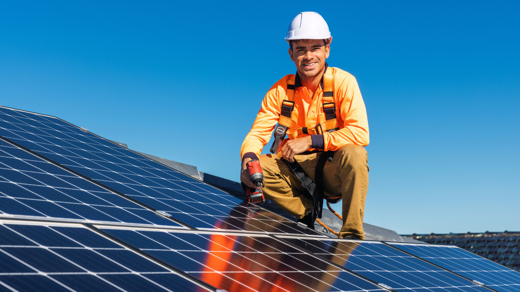 Solar photovoltaic installer working on rooftop solar panels while wearing a safety harness