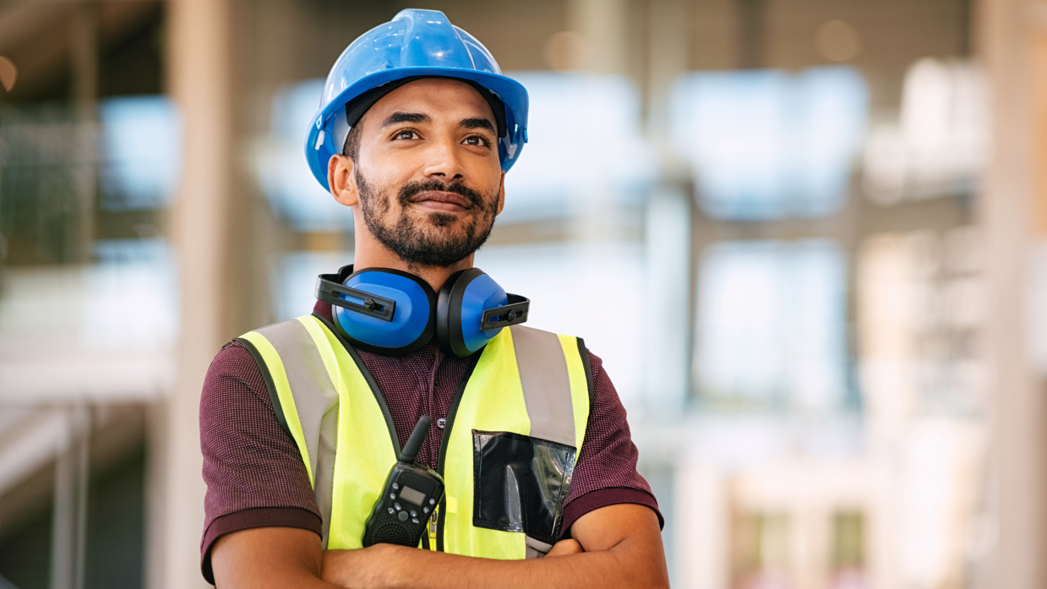 Trades worker wearing a hard hat and safety vest at a job site.