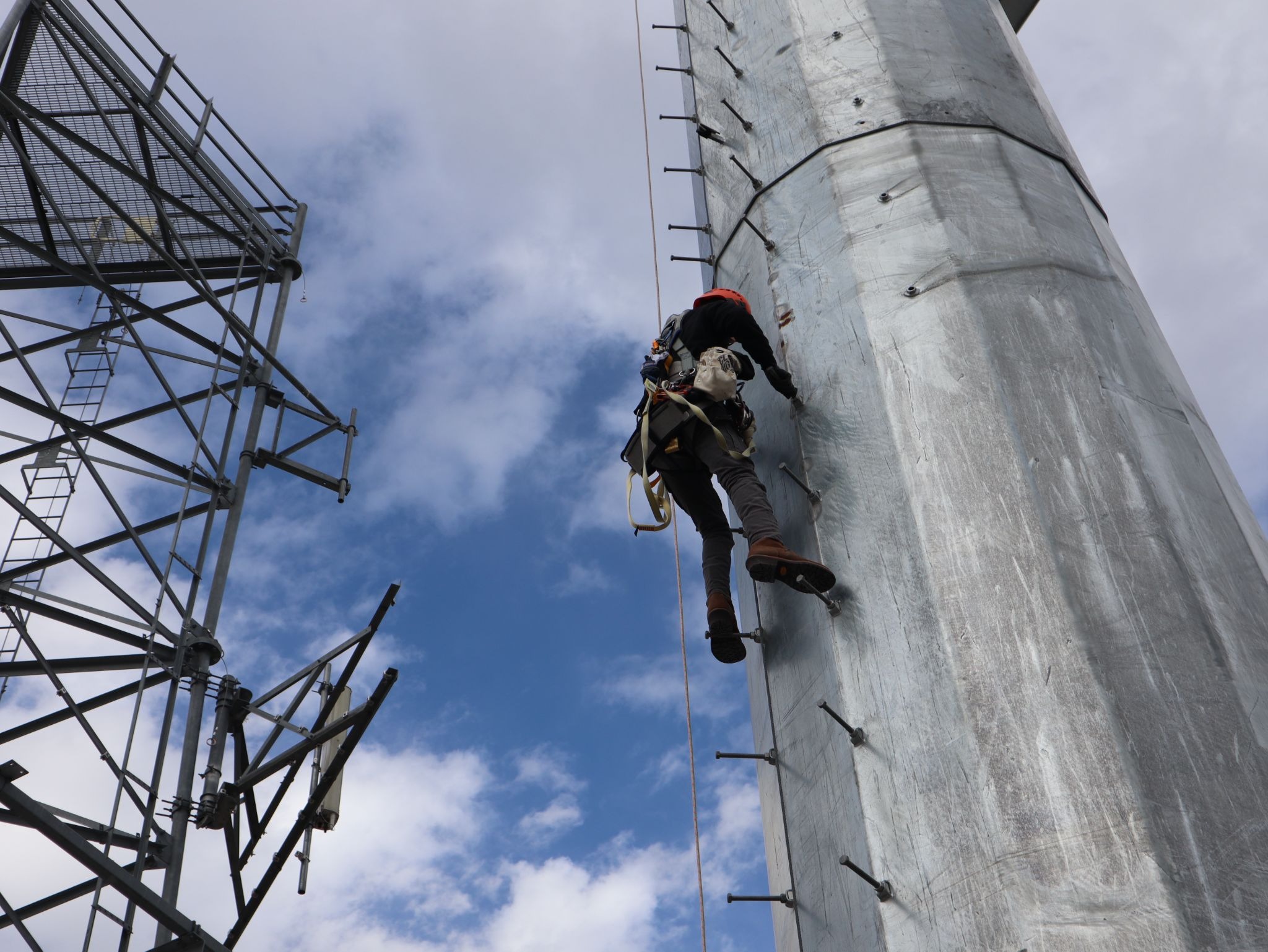 Wind turbine technician student climbing a training monopole tower during hands-on safety and climbing practice at Pinnacle Career Institute.