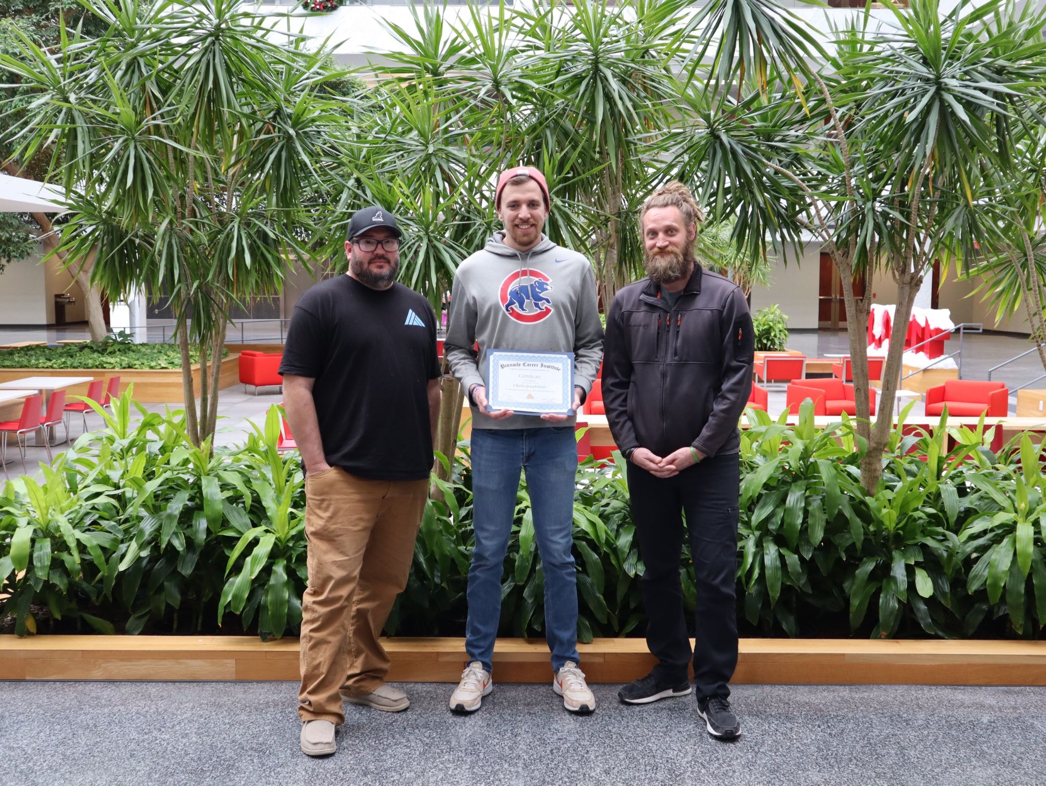 Trade school graduate holding a certificate alongside instructors at Pinnacle Career Institute campus.