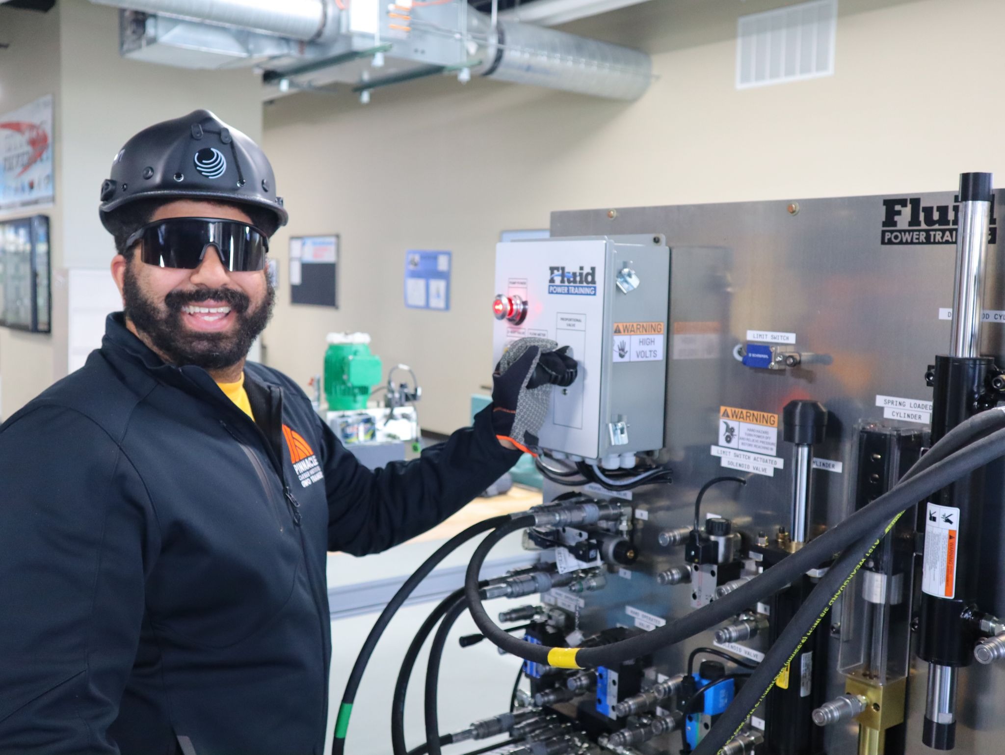 Trade school instructor wearing safety gear operating an electrical training panel in a hands-on lab at Pinnacle Career Institute.