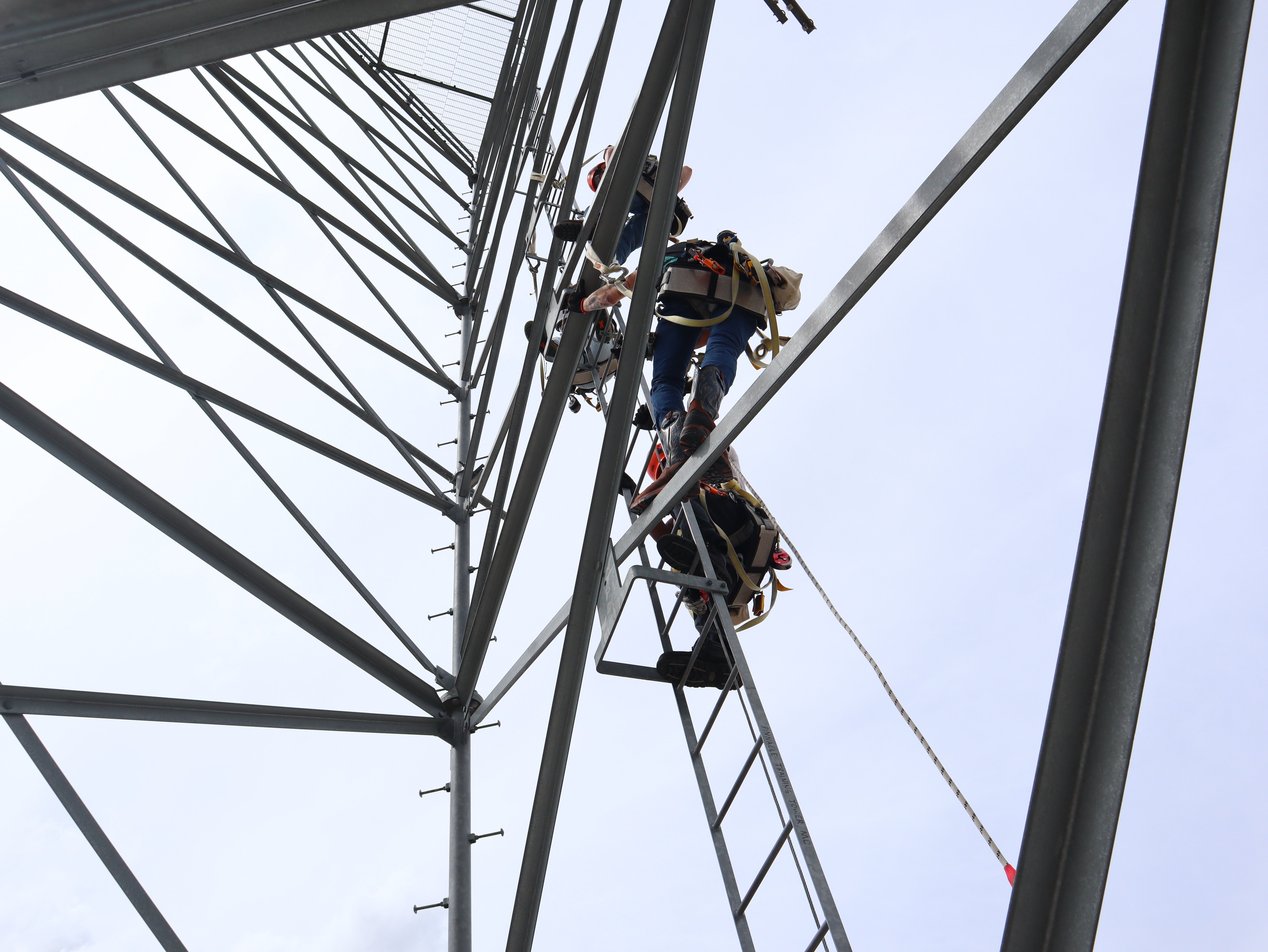 Pinnacle Career Institute students ascending a self-supporting telecommunications tower during hands-on training for PCI’s Tower Technician program, practicing climbing techniques and fall protection.
